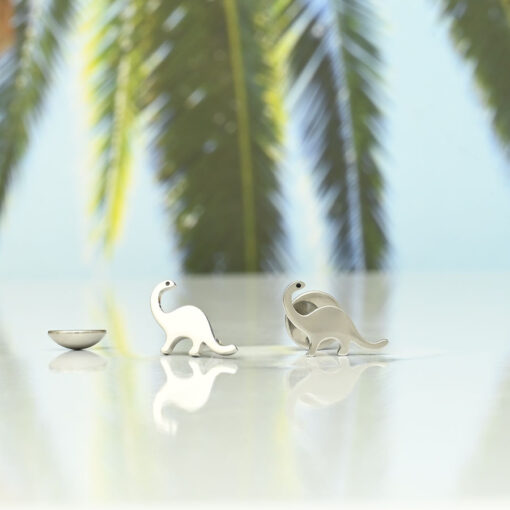 Dinosaur ComfyEarrings in 316L polished stainless surgical-grade steel pictured in front of a palm leaf background.