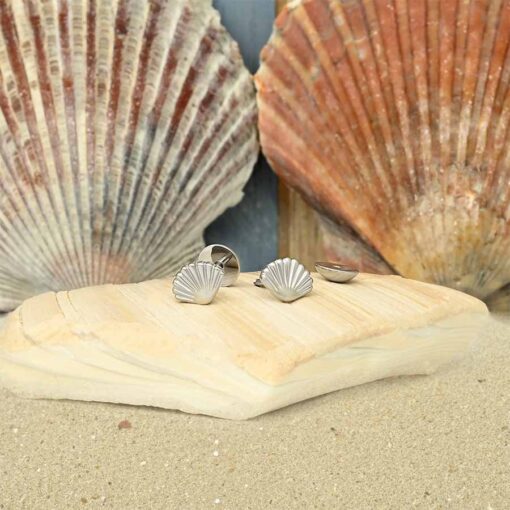 Seashell ComfyEarrings pictured on a shell, in front of other shells on sand.